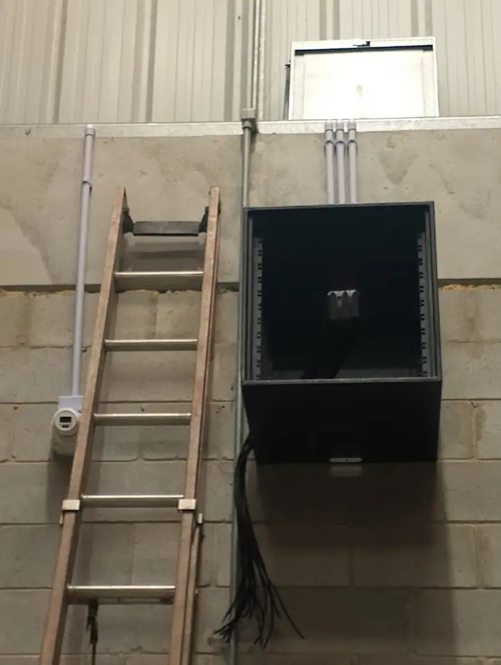 Caixa de equipamentos instalada em parede de bloco, com escada ao lado