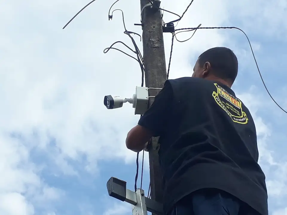 Técnico de uniforme GMTEL instalando câmeras no alto de um poste