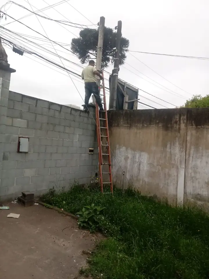 Técnico em escada instalando equipamento sobre muro