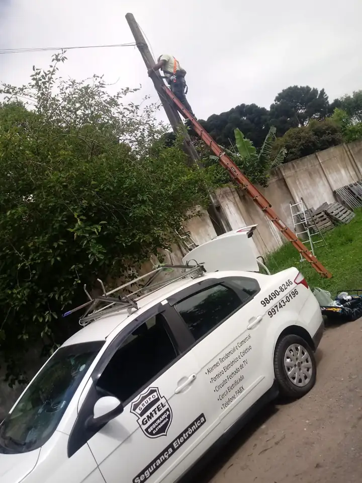 Técnico no alto do poste com o carro da GMTEL estacionado