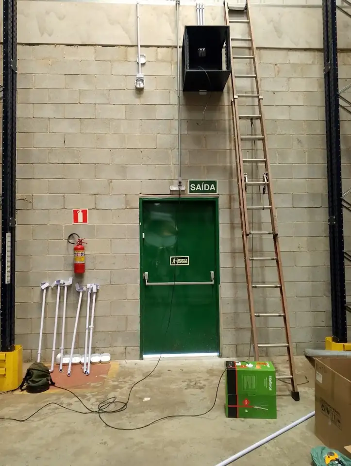 Parede alta de galpão com equipamento instalado e escada de acesso