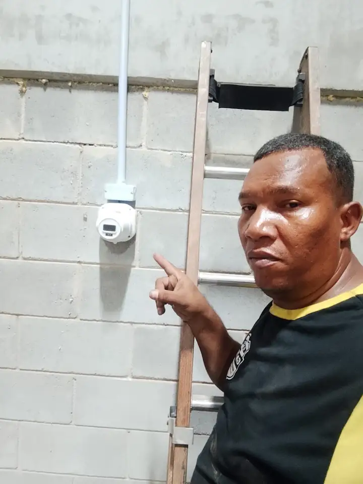 Técnico mostrando câmera recém instalada em parede de bloco